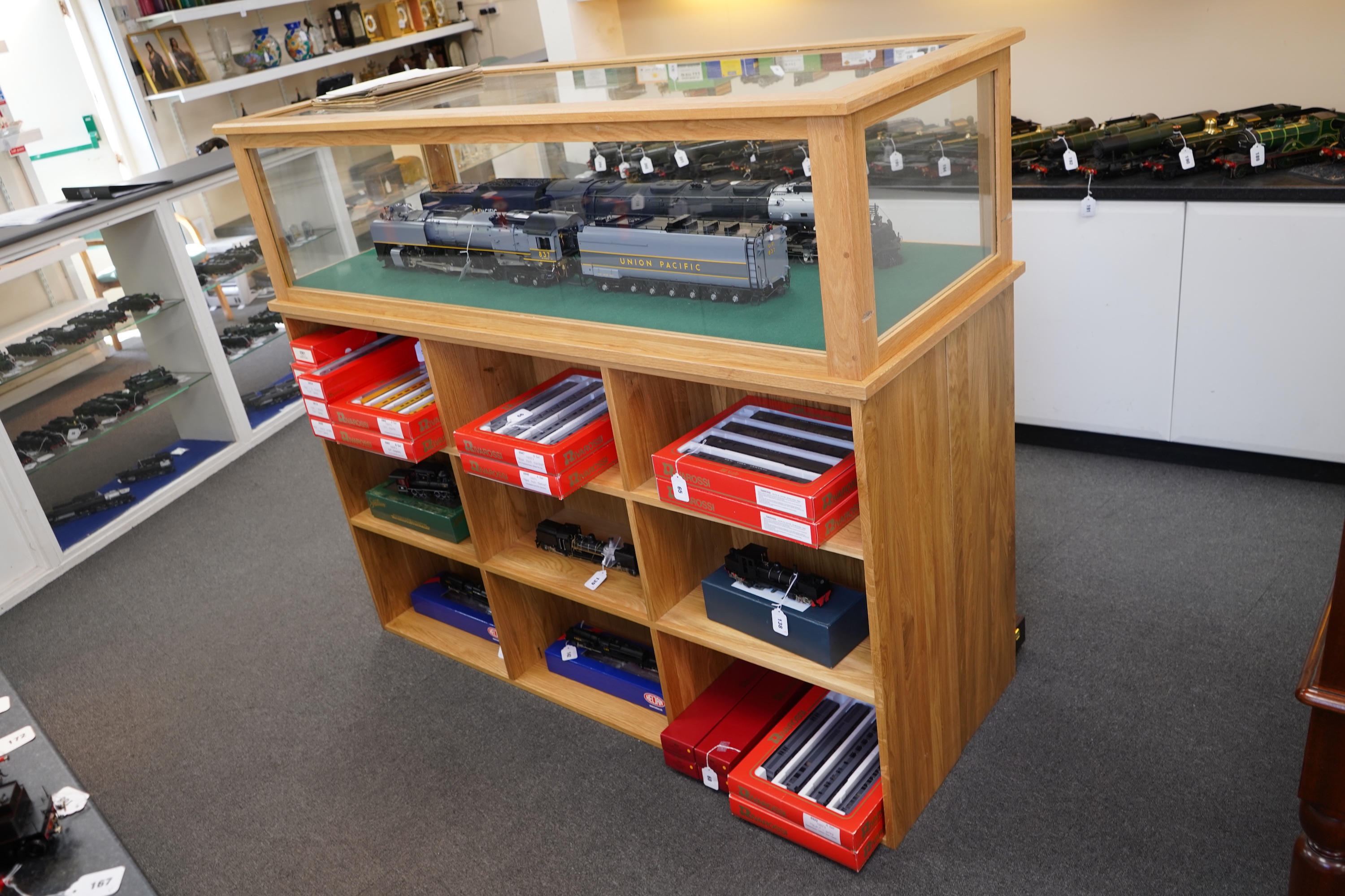 An engineered oak display stand, with a removable glazed top, and double sided base divided into nine compartments on each side, dimensions; 160cm wide, 60cm deep, 141cm high (contents for display purposes only and not i